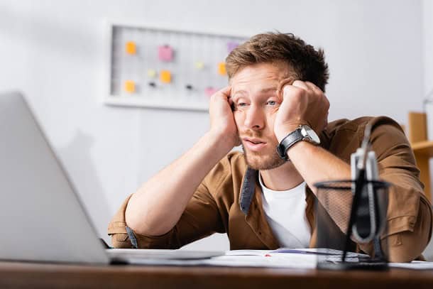 A man sitting in front of his laptop looking tired and unmotivated.