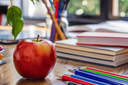 An apple and pens on a school desk.