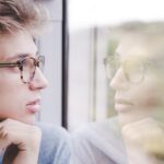 A man looking at his own reflection in the window of a train.