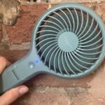 John Lewis Anyday fan in a hand, held in front of a brick wall